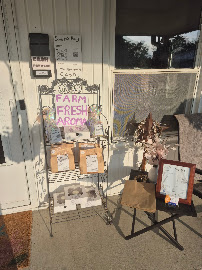 The Farm Fresh Aroma's self-serve stand on the porch, with bagged baked goods on a wire rack and a hand-lettered sign